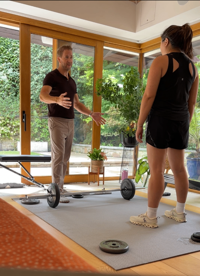Leigh Canning coaching a client through a barbell session in a private home gym